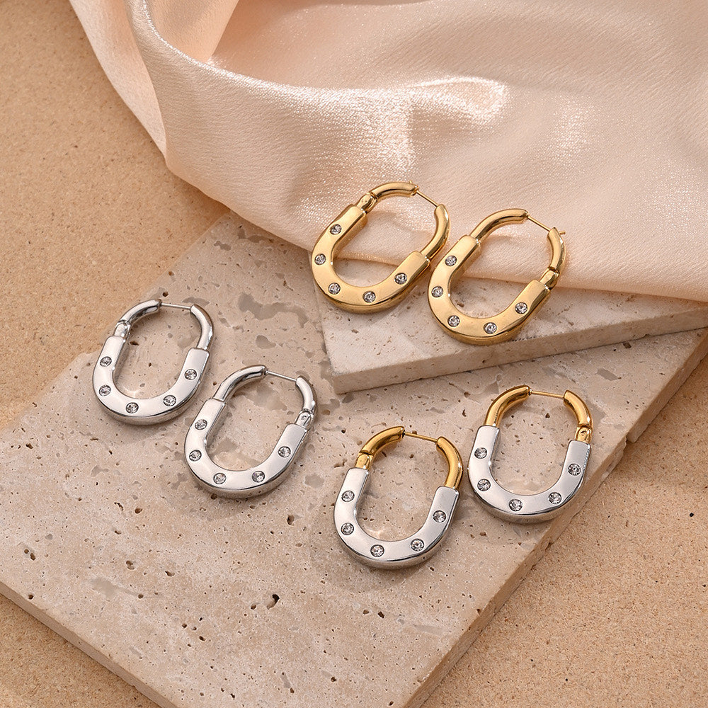 Pair of gold hoop earrings with small stones on a beige stone surface.